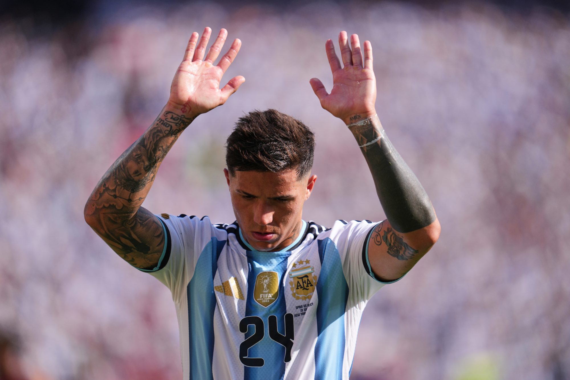 Argentine midfielder Enzo Fernández raising both hands to acknowledge the fans while wearing the Argentina national football team kit.